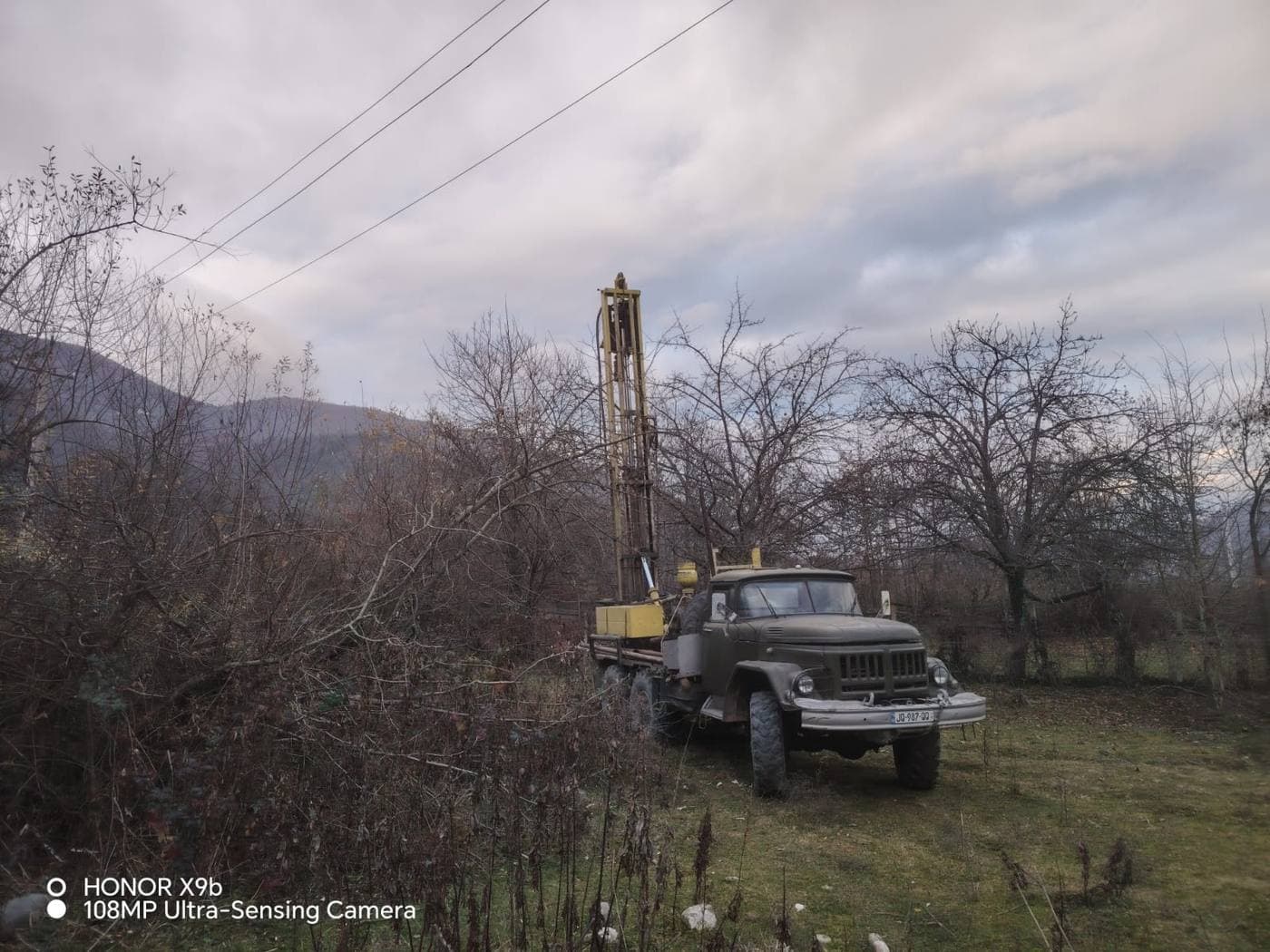 საბჭოური ტიპის მძიმე საბურღი დანადგარი მაღალი ანძით სოფლის ადგილზე ამბროლაურის მახლობლად შებინდებისას, რაჭის მთები ფონზე